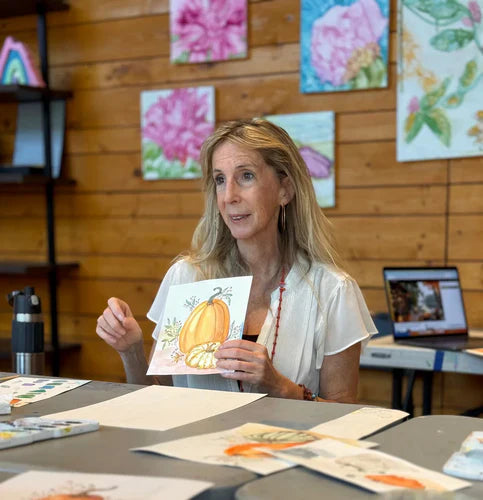 Tara Dickinson teaching a watercolor art class, holding a pumpkin painting