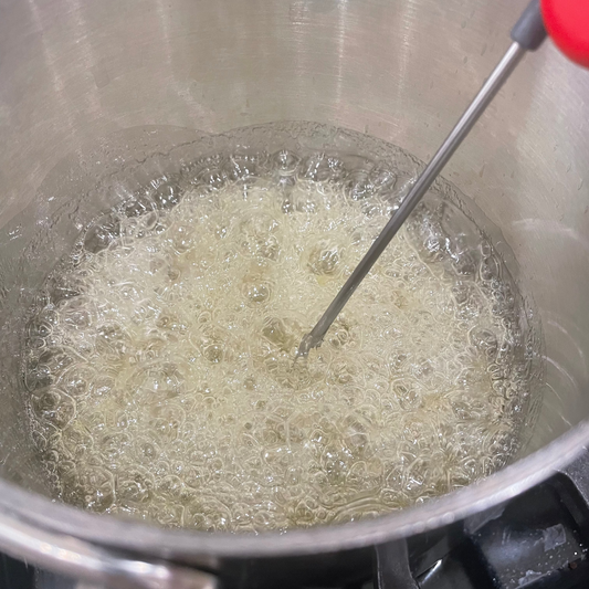 Bubbling liquid in a pot with a thermometer, likely during cooking or boiling.